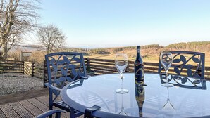 Une table avec deux verres à vin et une bouteille, placée devant un paysage rural pittoresque.