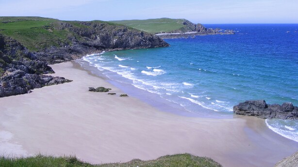 Un paysage côtier avec une plage de sable, des falaises rocheuses et une mer bleue et limpide.