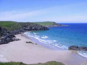 A coastal landscape with a sandy beach, rocky cliffs, and a clear blue sea. - A converted barn ideally situated for exploring the fabulous Highlands. (Lairg)