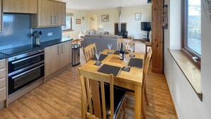 Une cuisine moderne dotée de fours encastrés, un coin repas avec une table et des chaises en bois, et un salon avec un canapé et une télévision.