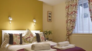Een net opgemaakt bed met een rode deken, twee bedlampjes en een bloemendecoratie gordijn.