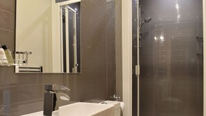 Een moderne badkamer met een douchecabine van glas, een witte wastafel en een spiegel erboven.
