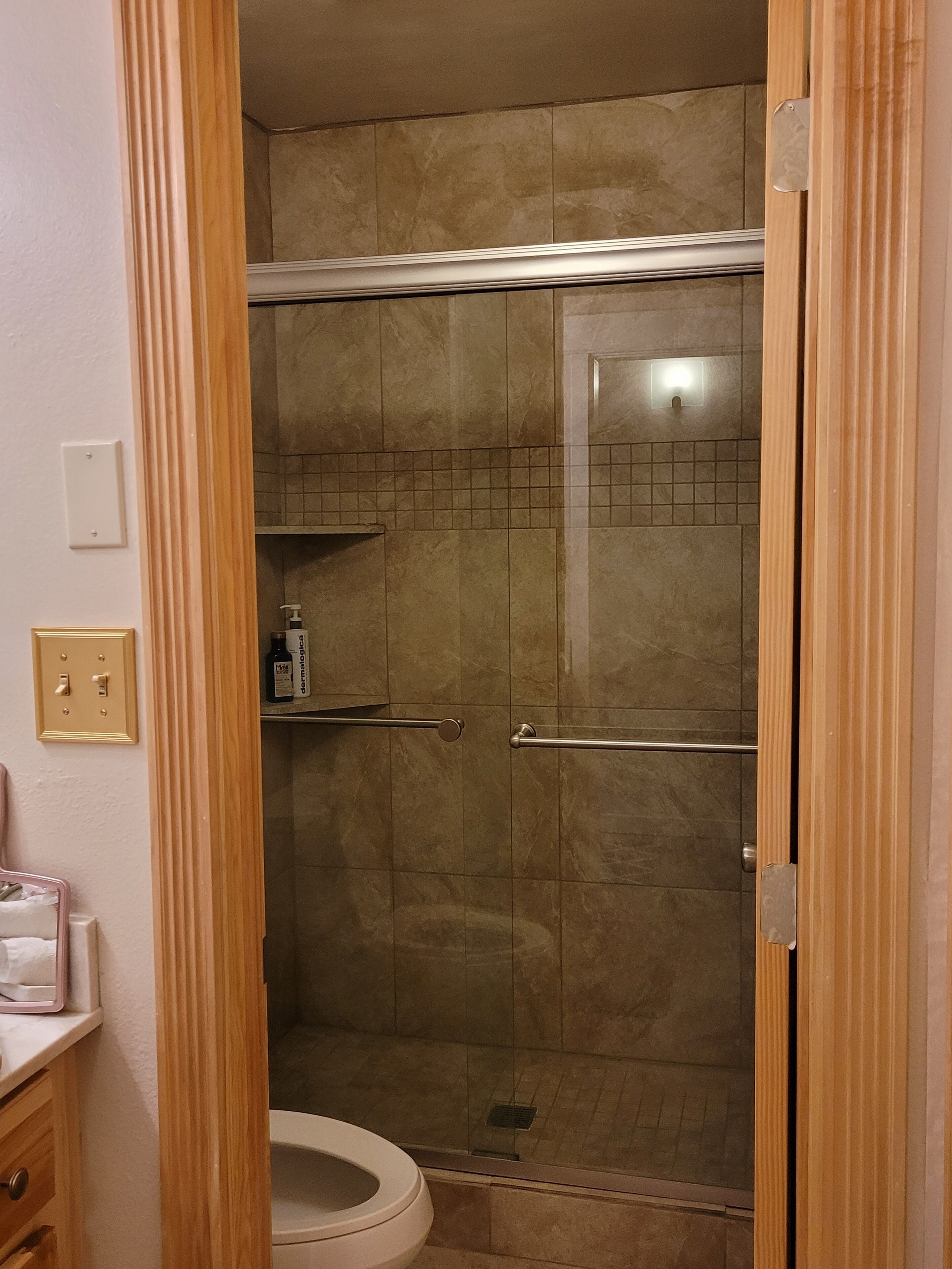 A bathroom with a shower, toilet, and a shelf with toiletries.