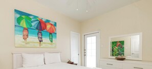 A bedroom with a bed, a painting of umbrellas, a door, and a mirror.