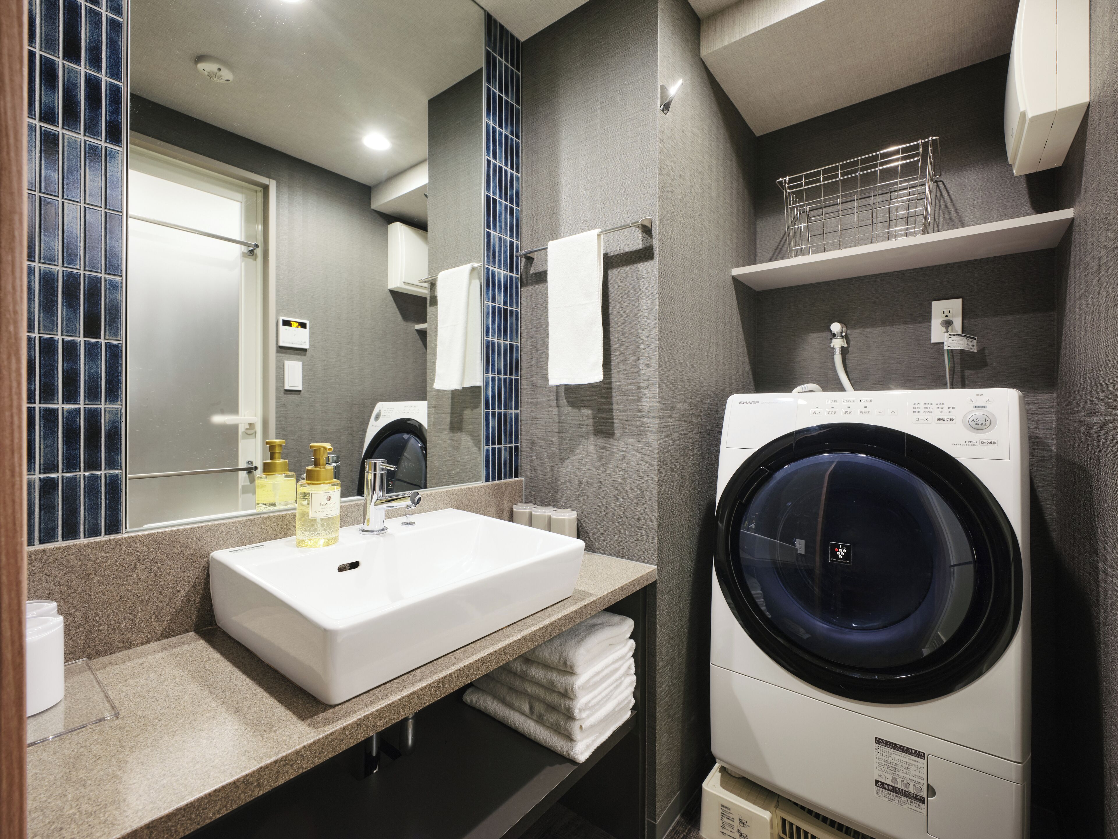 A modern bathroom with a sink, mirror, and a front-loading washing machine.