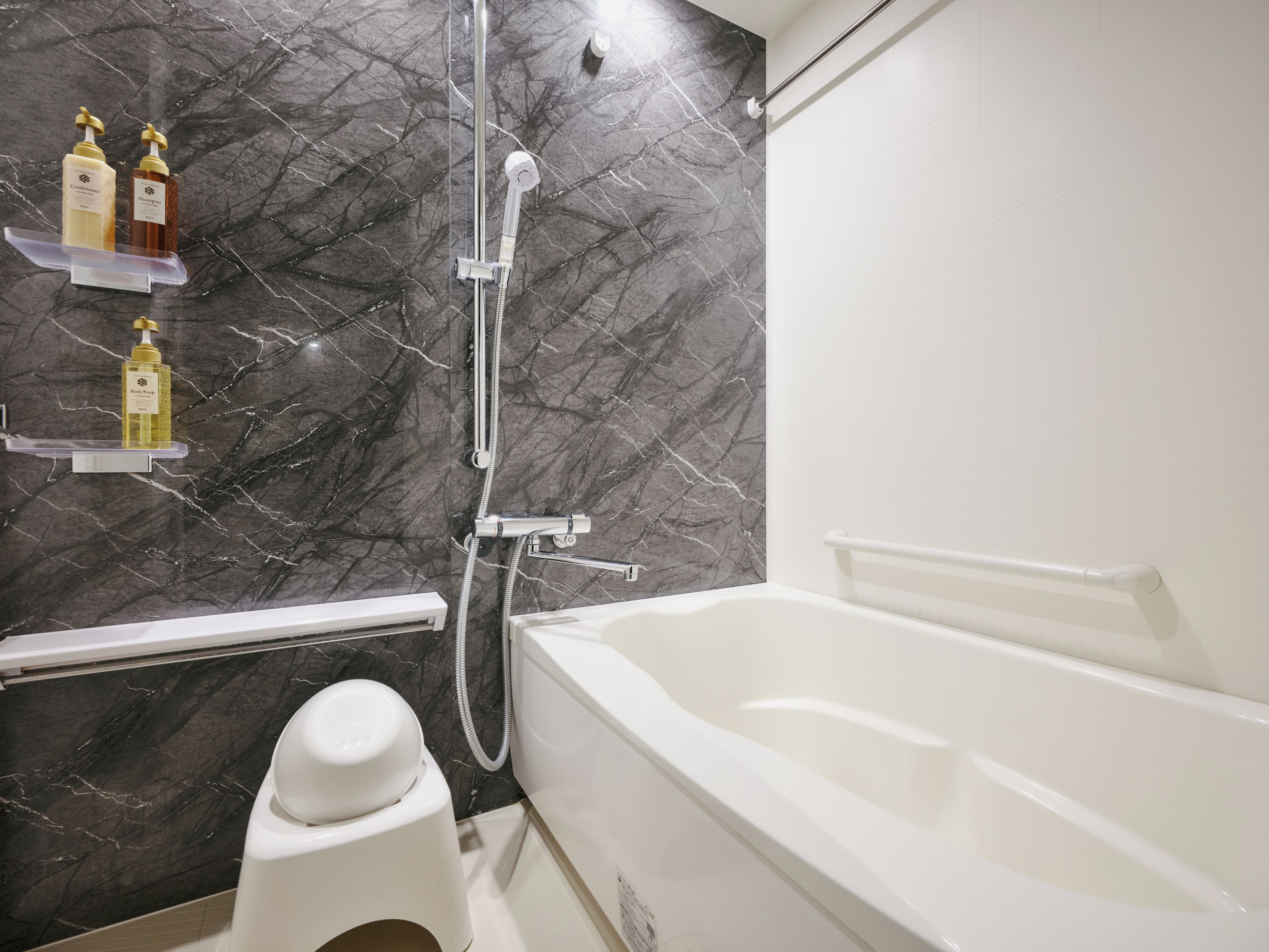 A bathroom with a bathtub, a shower, and a toilet. There are shelves with toiletries on the wall.