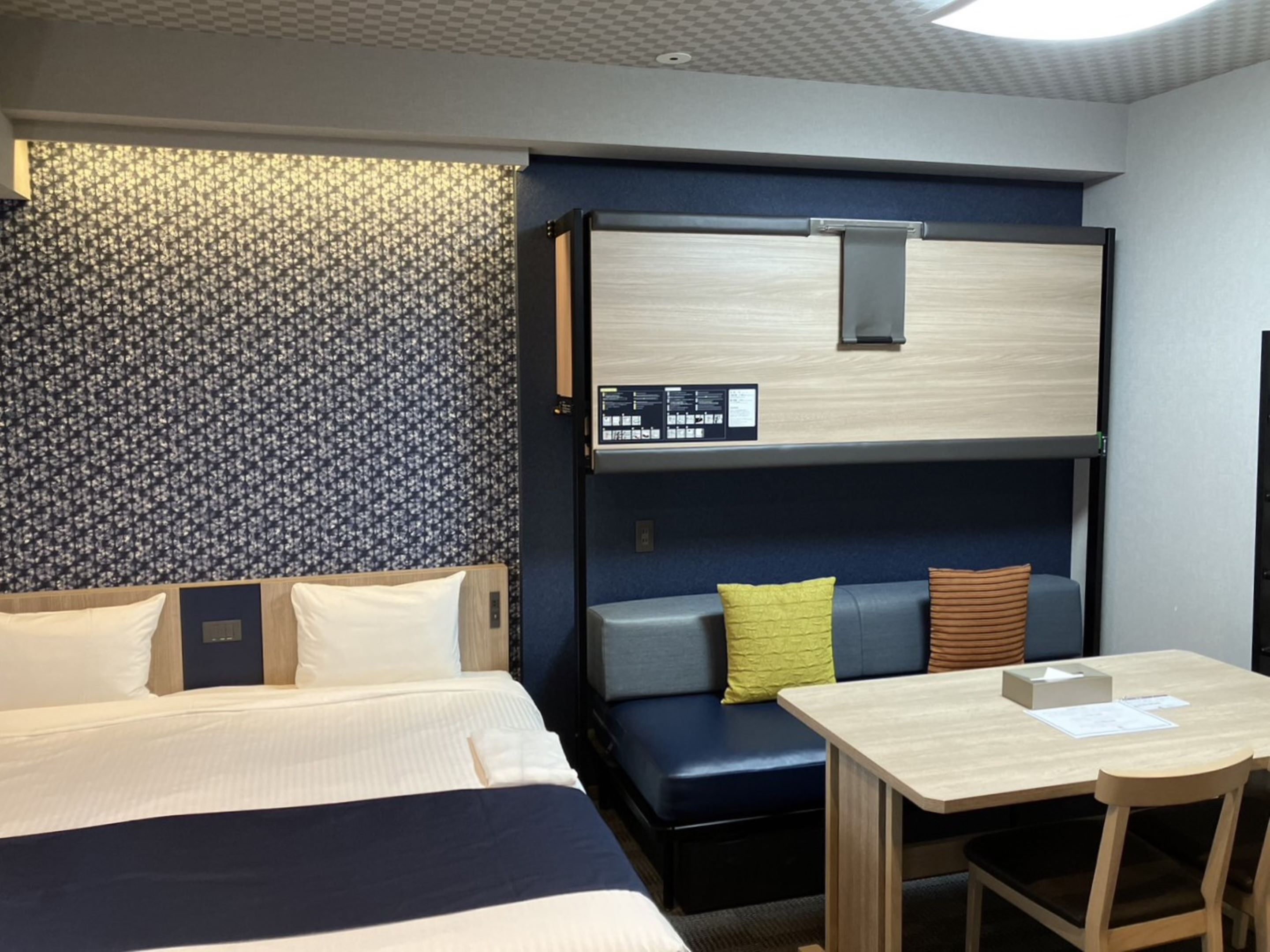 A hotel room with a bed, a desk, and a seating area with cushions.