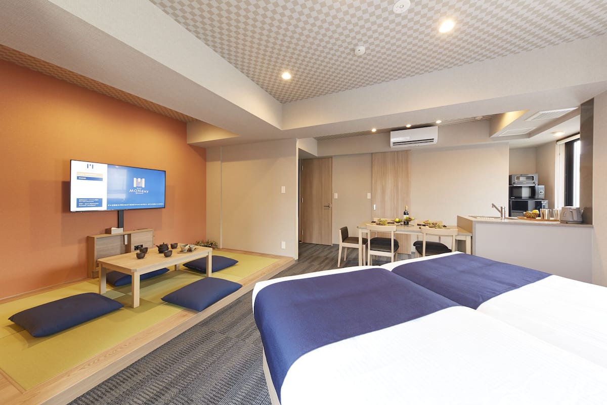 Hotellihuone, jossa on sänky, työpöytä, televisio ja pieni keittiönurkkaus.