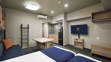 A hotel room with two beds, a desk, a kitchenette, and a TV.