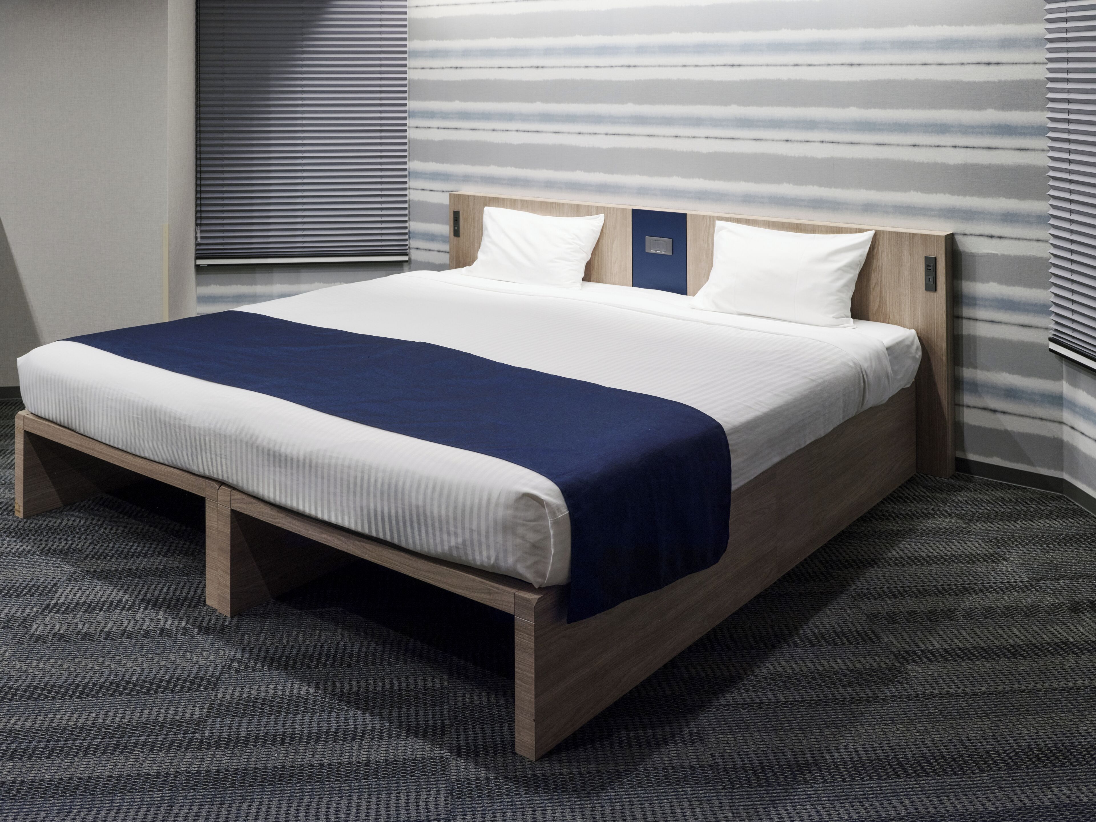 A neatly made bed with a wooden frame, white and blue bedding, and a striped wall behind it.
