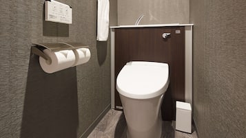 Une salle de bain moderne équipée de toilettes, d’un distributeur d’essuie-tout et d’une petite poubelle.