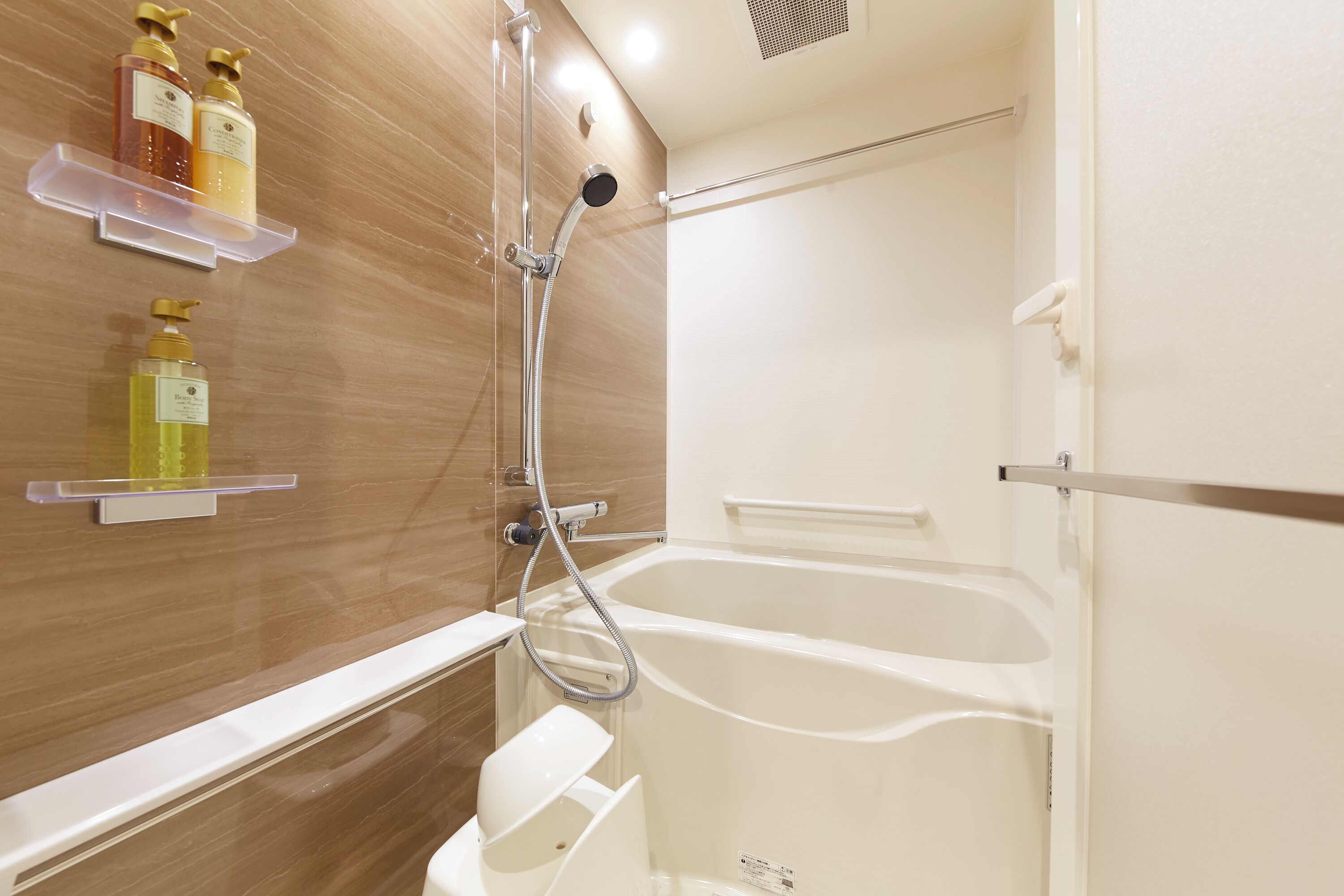 Et badeværelse med badekar, bruser og hylder med toiletartikler.
