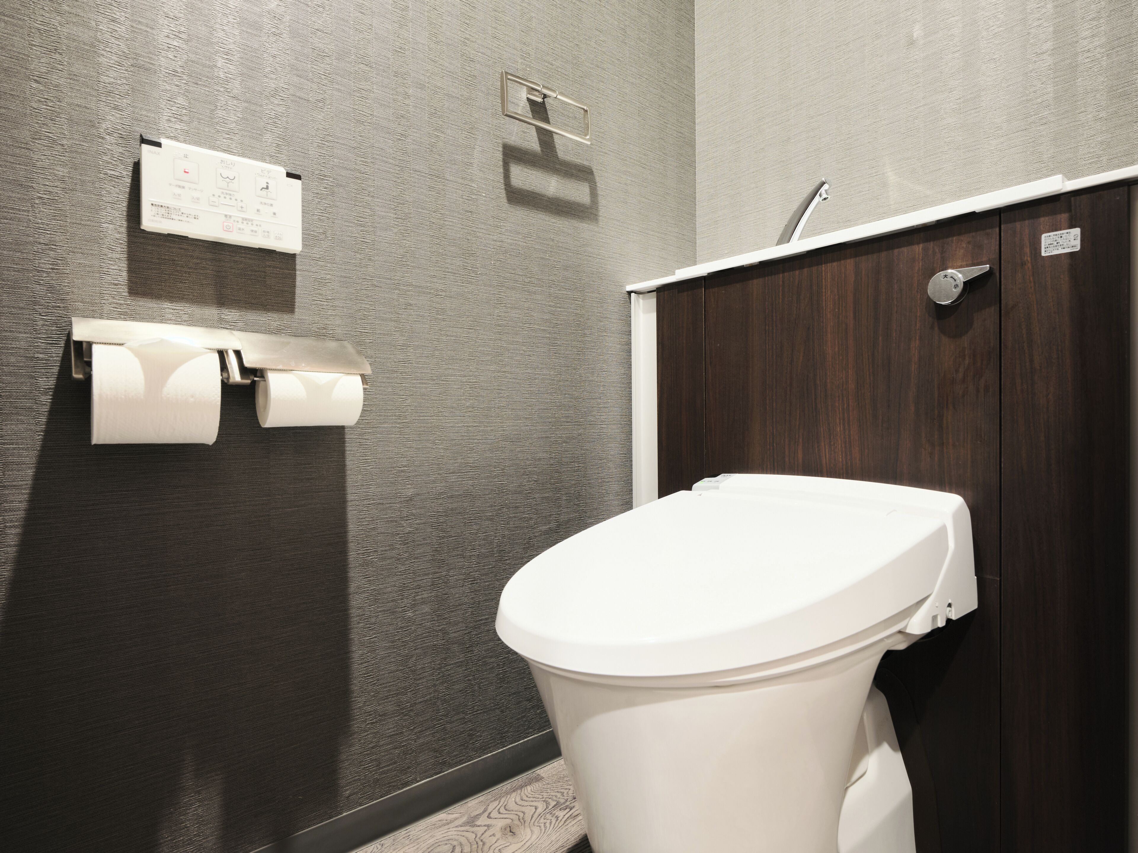 A modern bathroom with a toilet, a paper towel dispenser, and a wooden cabinet.