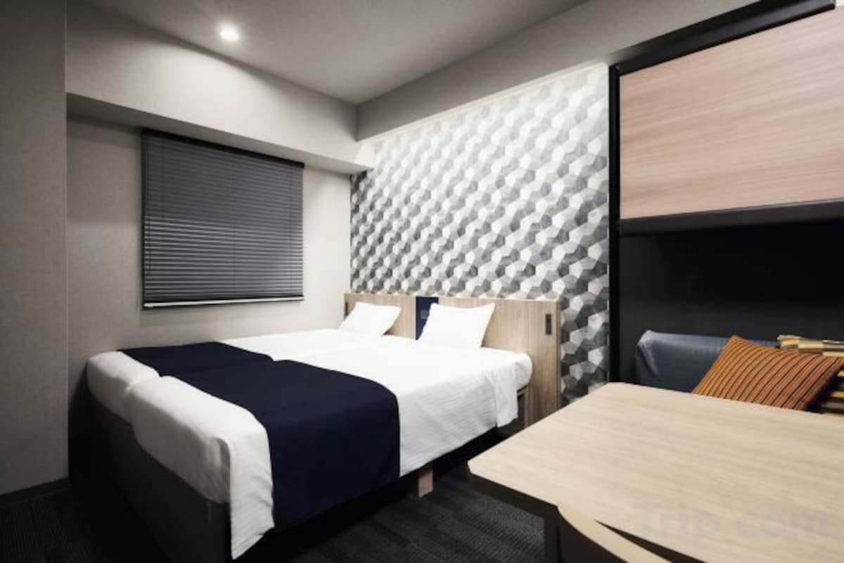 A hotel room with a bed, a desk, and a window with blinds.