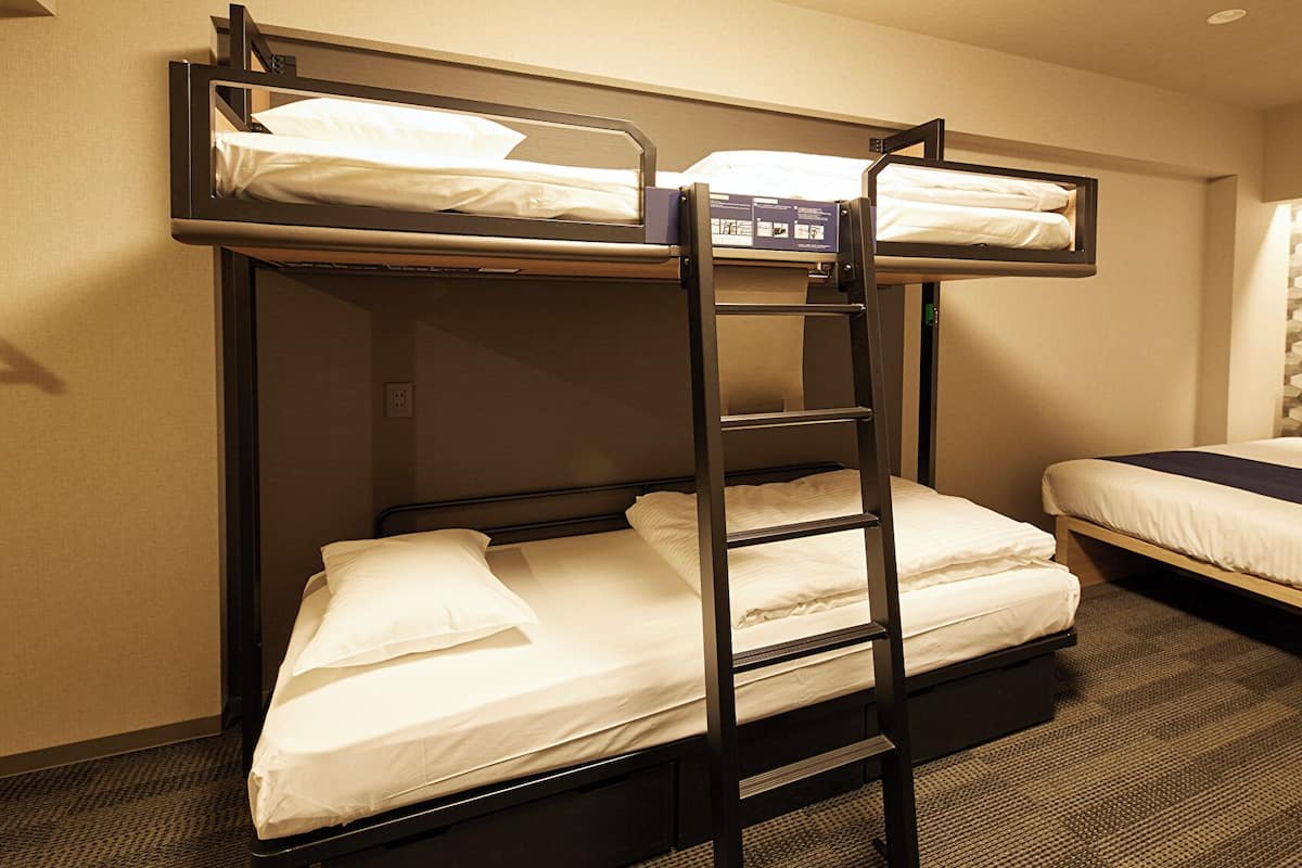 A bunk bed room with a ladder, a single bed, and a wall-mounted information board.