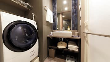 A compact hotel bathroom with a front-loading washing machine, a sink with a mirror above, and a towel rack.