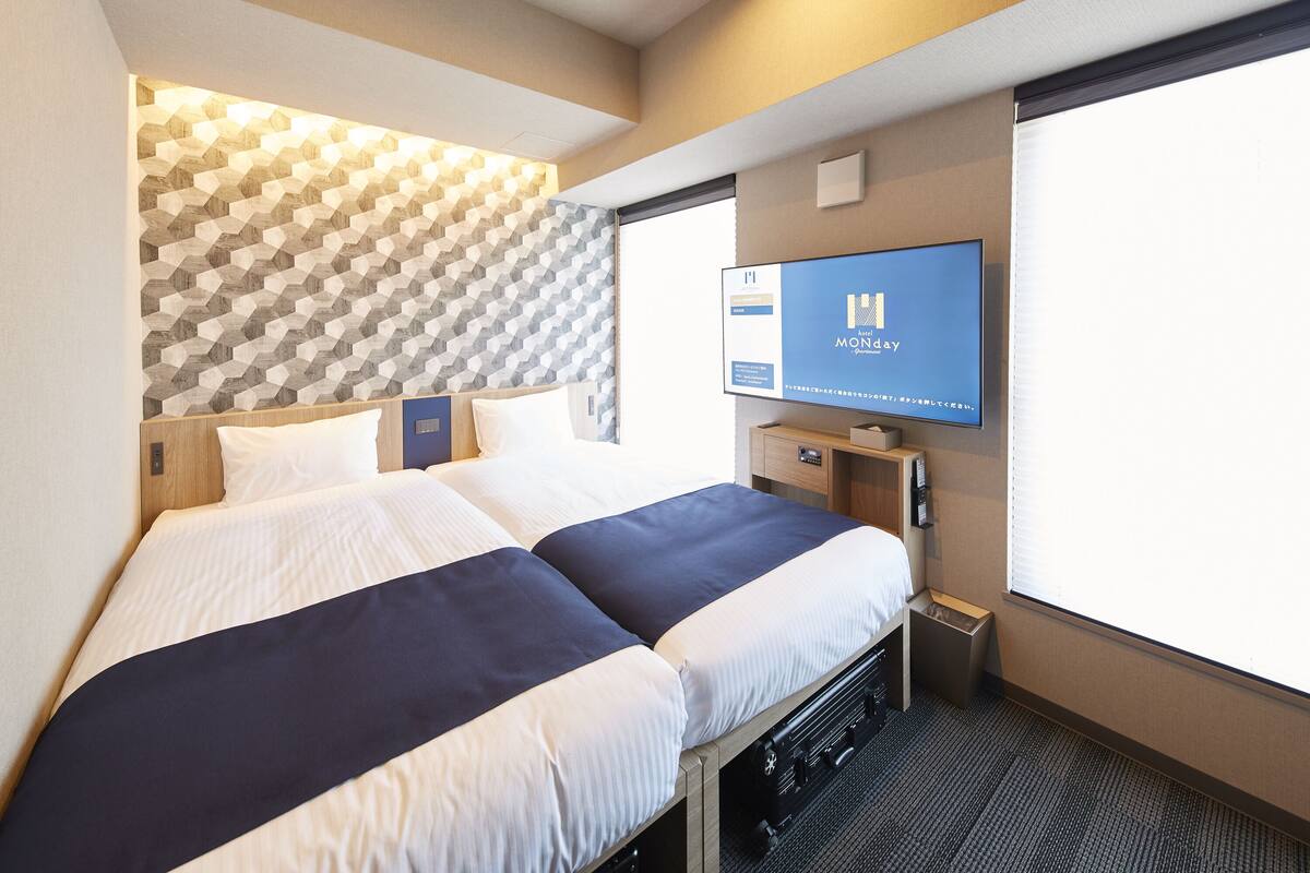 A hotel room with a bed, a television, and a window.