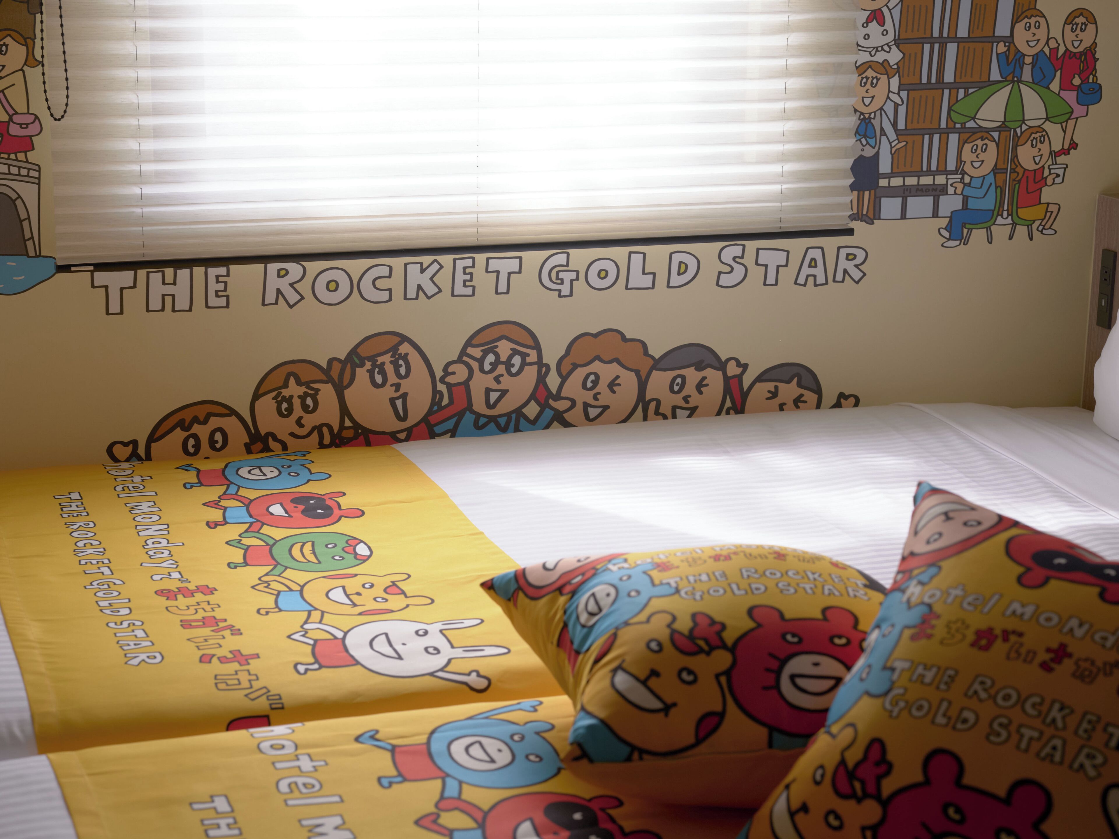 Quarto de hotel com cama, almofadas e um mural de personagens de desenho animado.