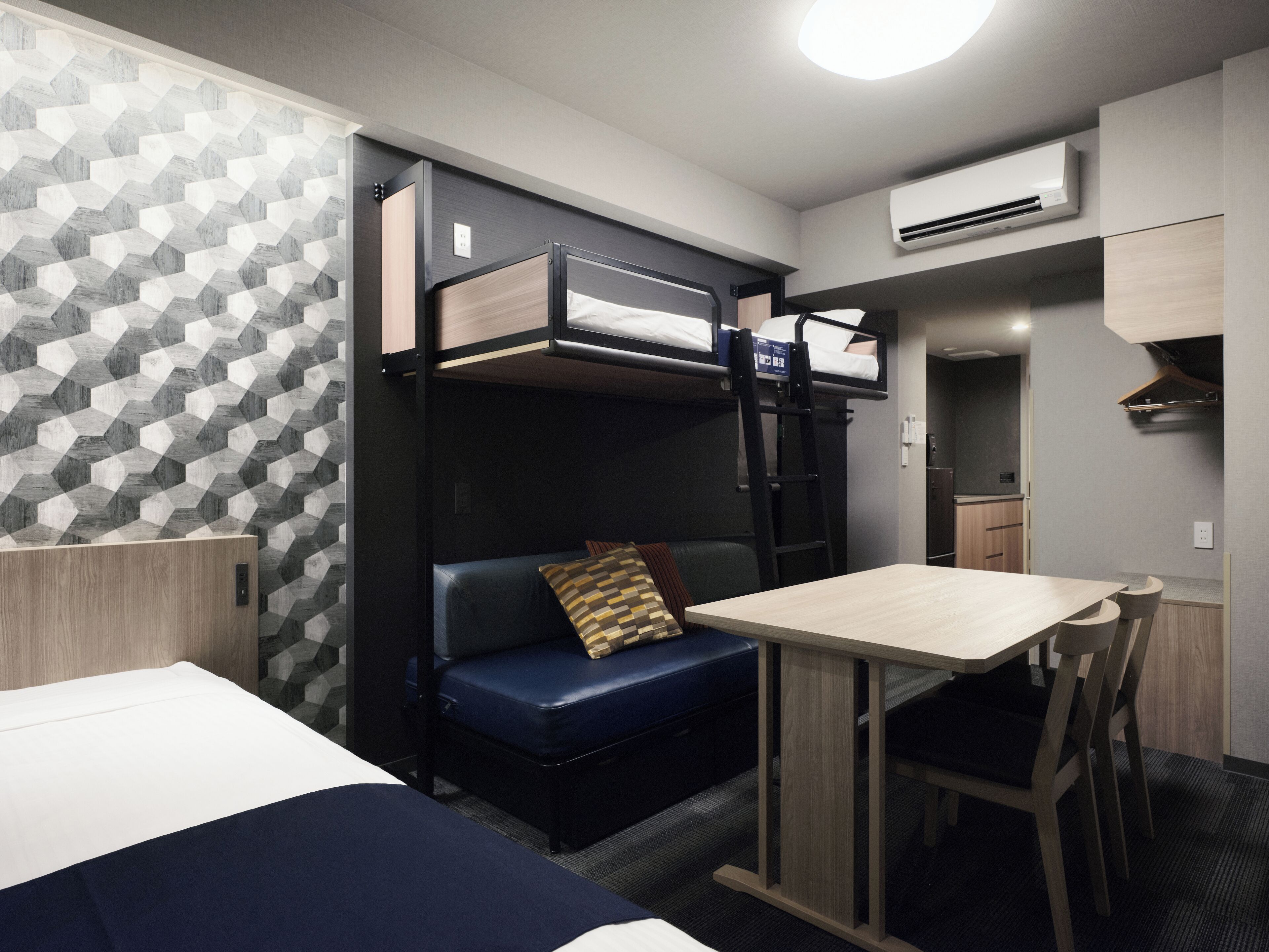 Ein kleines Zimmer mit Etagenbetten, einer Sitzecke, einem Tisch und einer Küchenzeile.