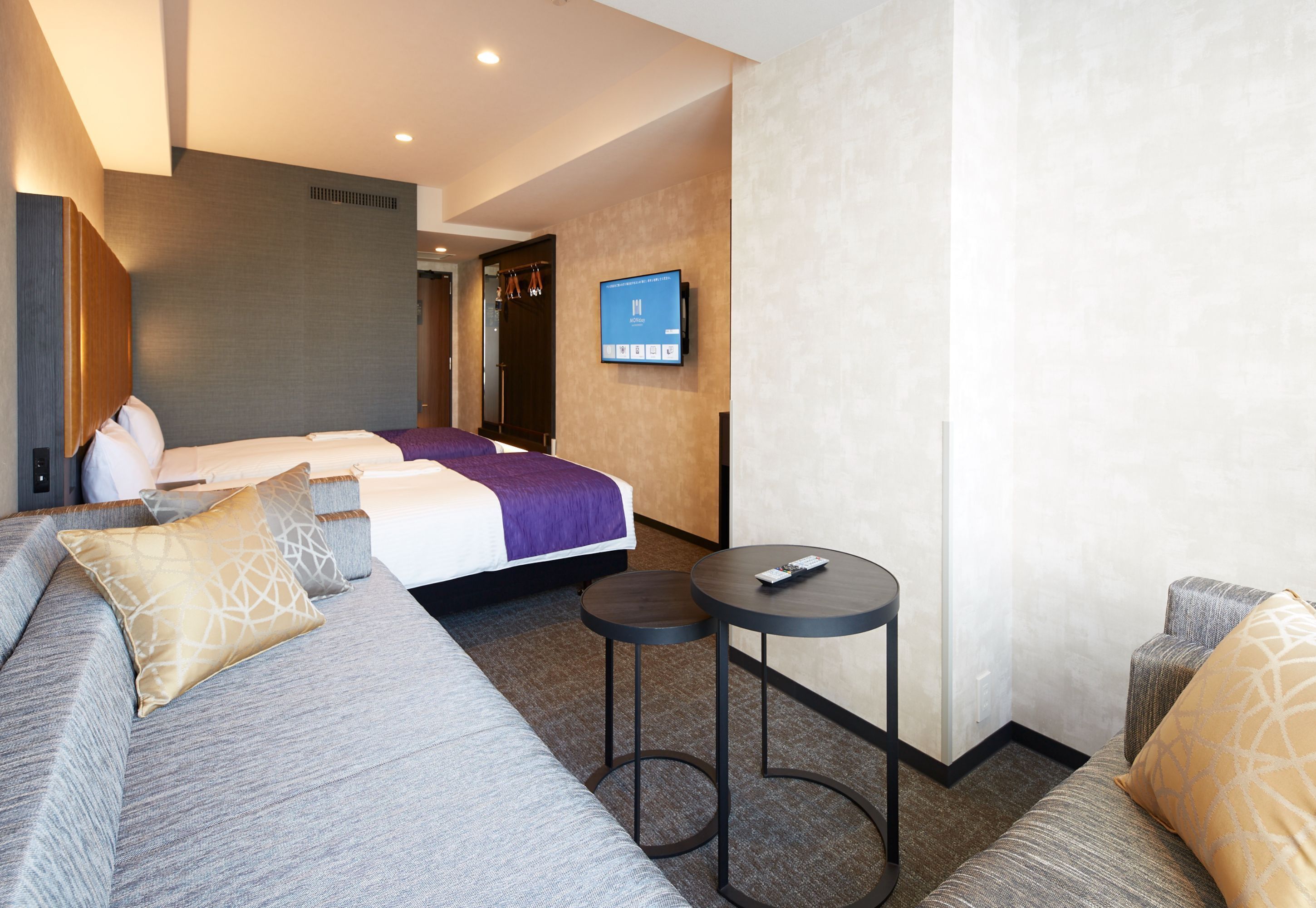 A hotel room with a bed, a sofa, a small table, and a TV mounted on the wall.