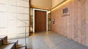 A modern hotel lobby with a herringbone-patterned wall, a wooden door, and a staircase with tactile paving. - hotel MONday Kyoto Marutamachi (Kyoto)