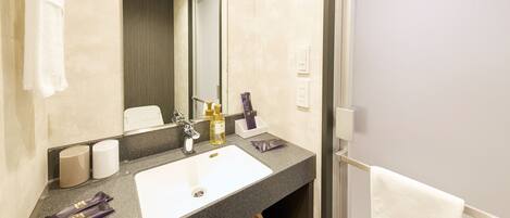 A hotel bathroom with a white sink, dark countertop, and a mirror.
