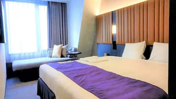 Une chambre d’hôtel avec un grand lit, un lit plus petit, un bureau et une fenêtre avec des rideaux.