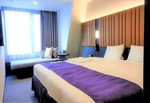 Una habitación de hotel con una cama grande, una cama más pequeña, un escritorio y una ventana con cortinas.