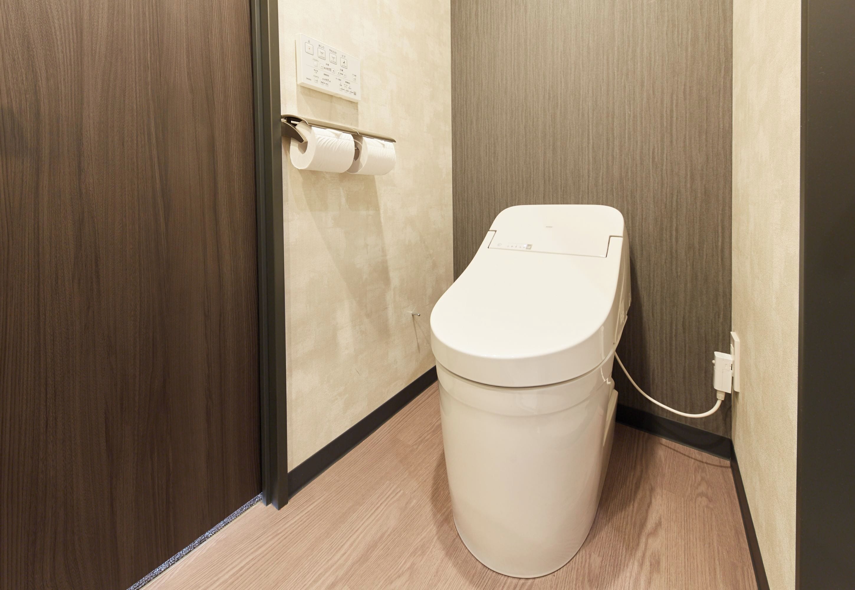 Ein kleines, modernes Badezimmer mit Toilette, Toilettenpapierhalter und einem fest installierten Steckdosenanschluss.