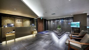A modern reception area with a reception desk, a seating area with chairs, a large flat-screen TV, and a decorative wall. - hotel MONday Kyoto Marutamachi (Kyoto)