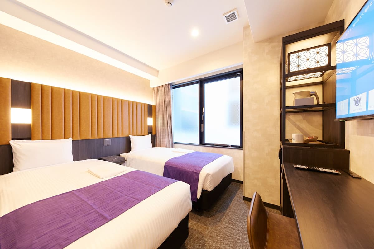 A hotel room with two beds, a desk, a TV, and a window with a view.