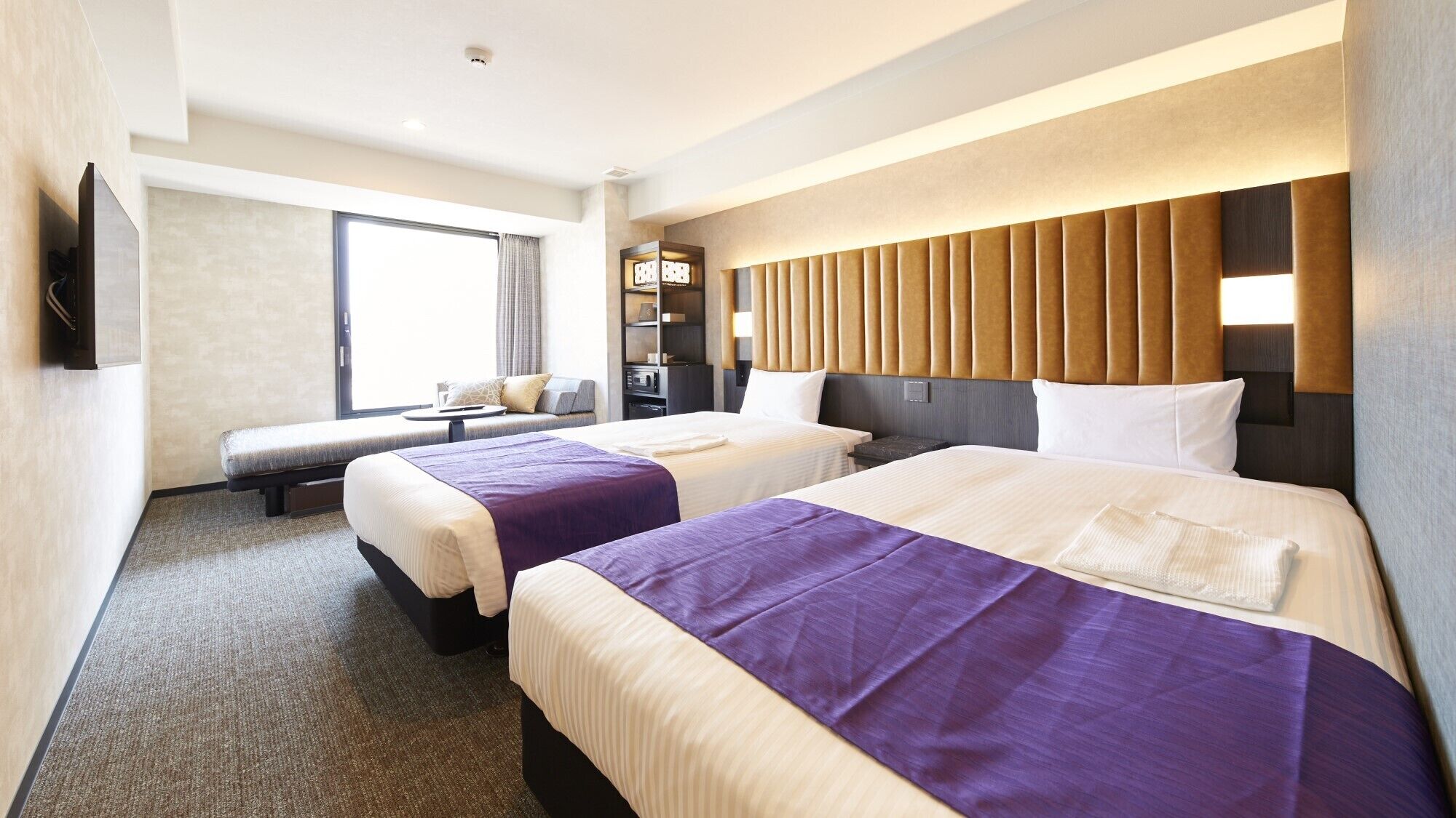 Quarto de hotel com duas camas, um sofá, uma televisão e um mini-bar.