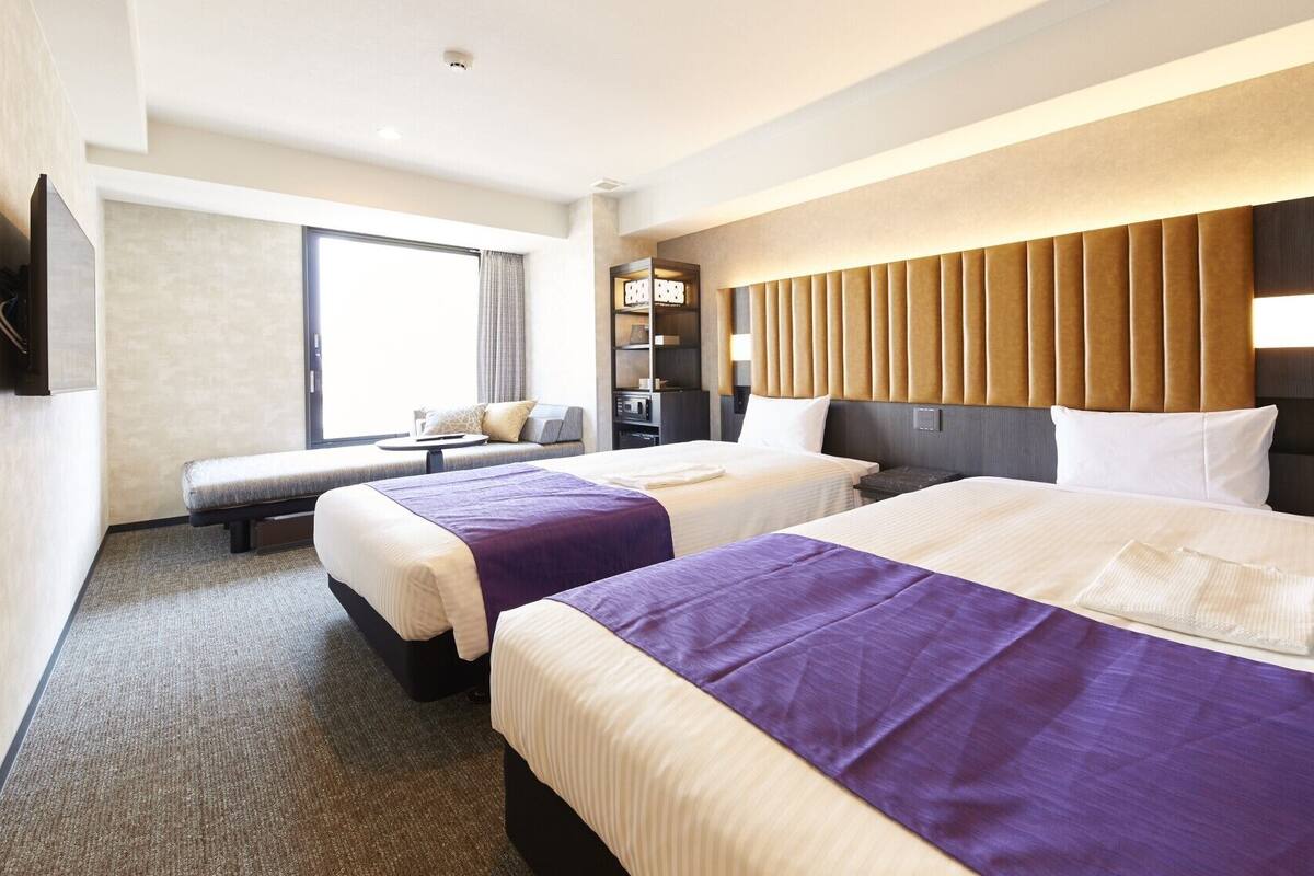 Habitación de hotel con dos camas, un sofá, televisión y minibar.