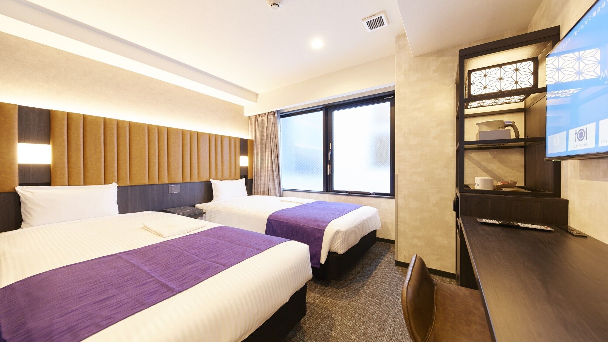 Quarto de hotel com duas camas, uma escrivaninha, televisão e janela.