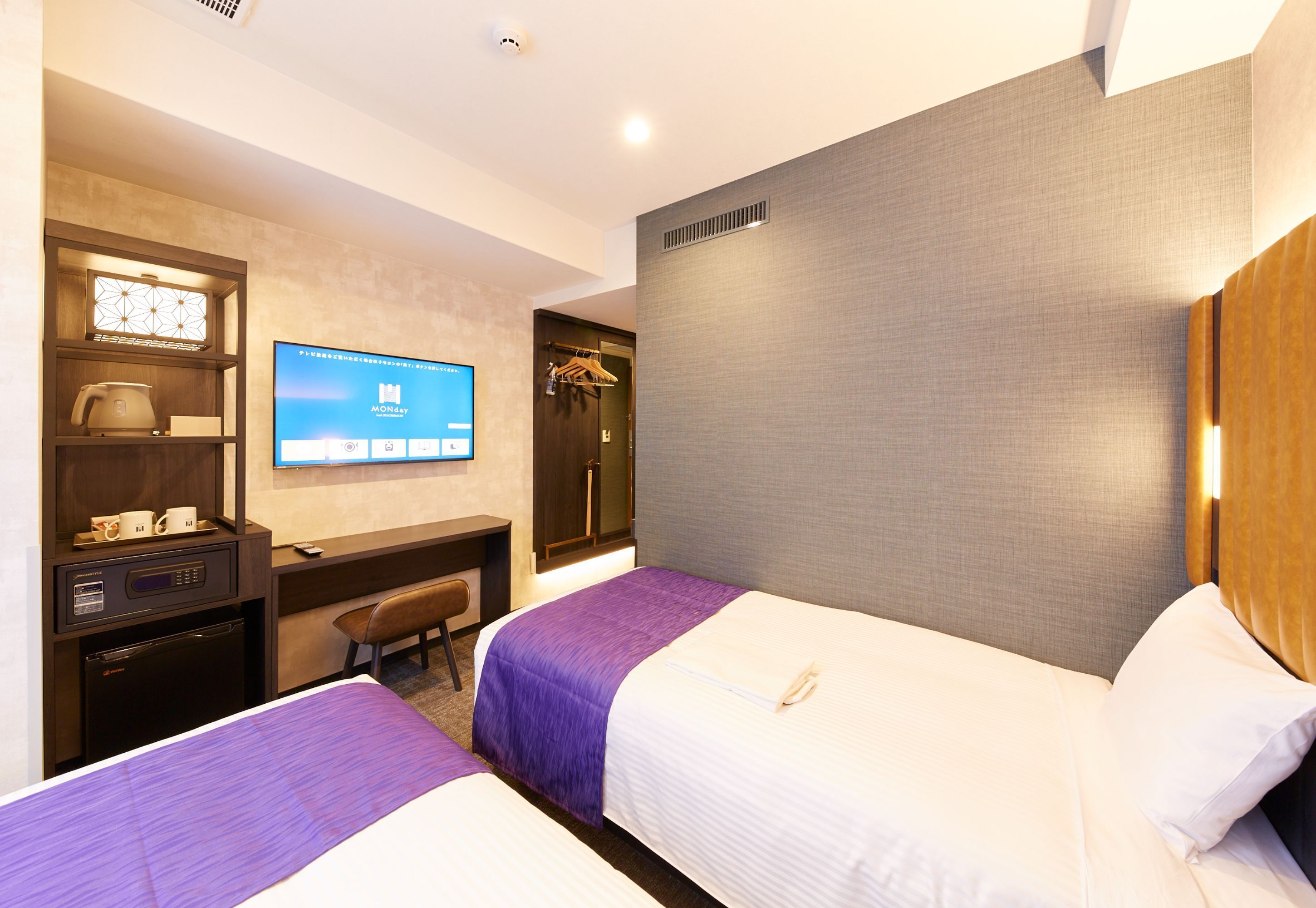 A hotel room with two beds, a desk with a computer, a television, and a minibar.
