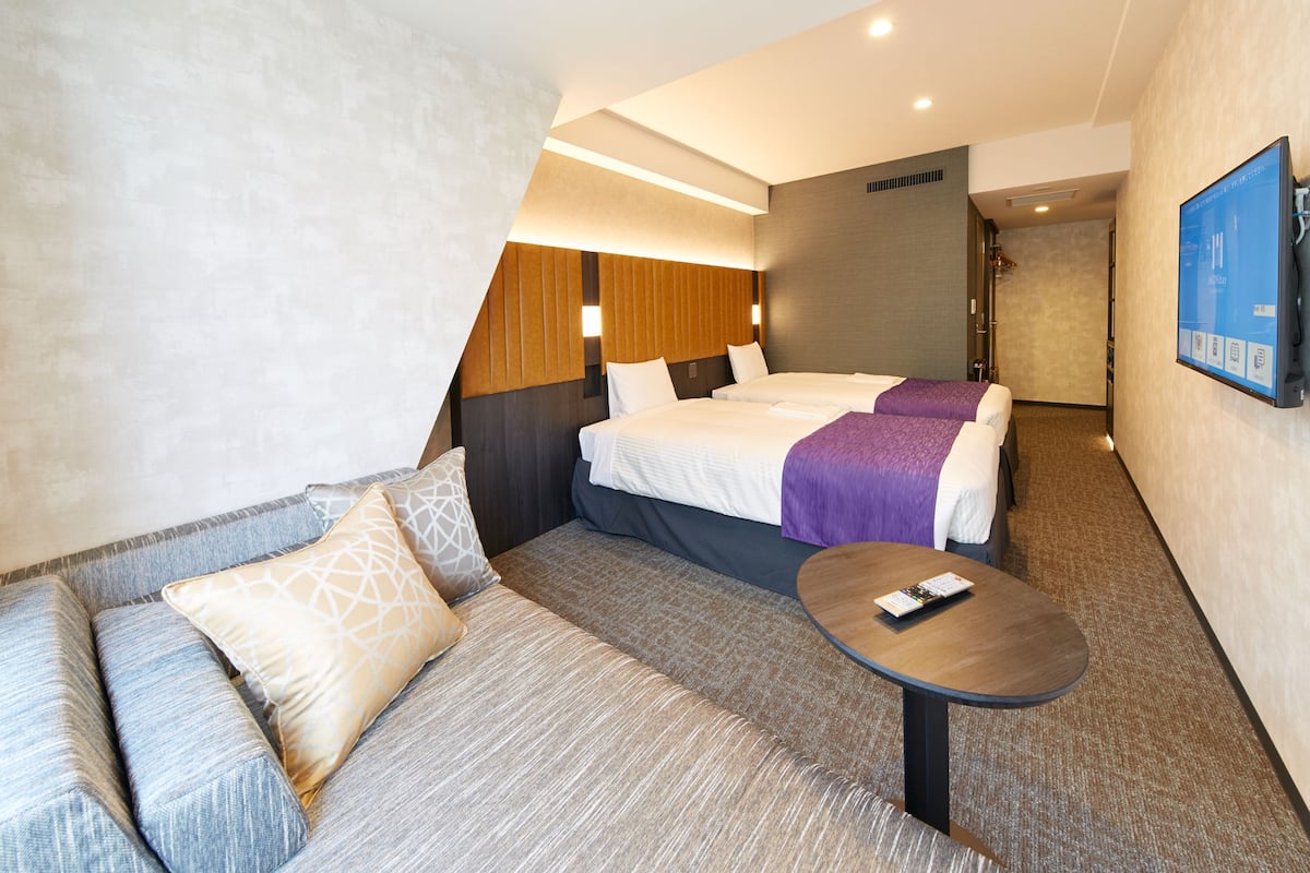 A hotel room with a sofa, two beds, a small table, and a TV.
