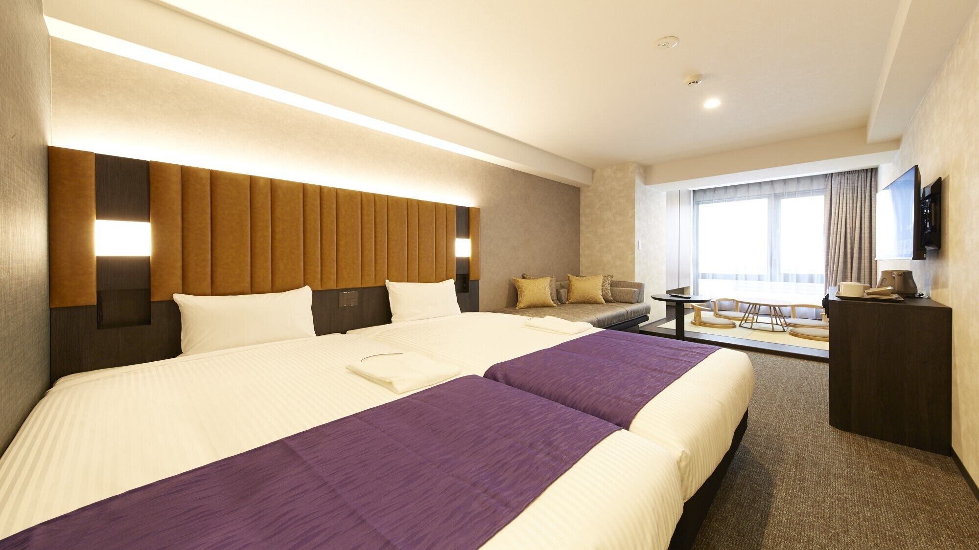 Quarto de hotel com uma cama grande, um sofá, uma mesinha e uma televisão.