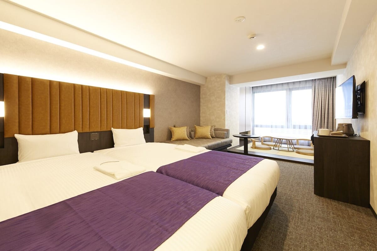 Habitación de hotel con una cama grande, un sofá, una mesita y un televisor.
