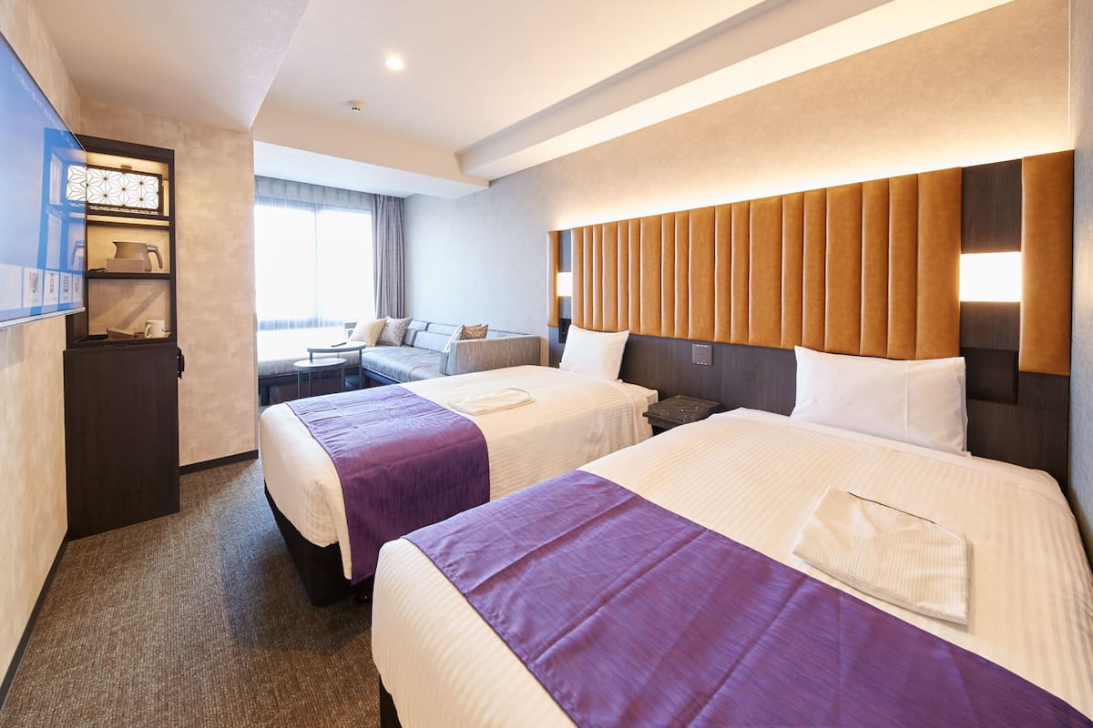 A hotel room with two beds, a desk, a chair, and a large window.