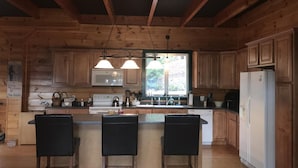 A wooden cabin-style kitchen with a central island, bar stools, wooden cabinets, and a refrigerator. - Direct Snowmobile and ATV trail from front door (Colebrook)