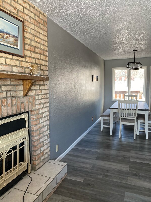 A living room with a brick fireplace, grey walls, and a dining area with a table and chairs.