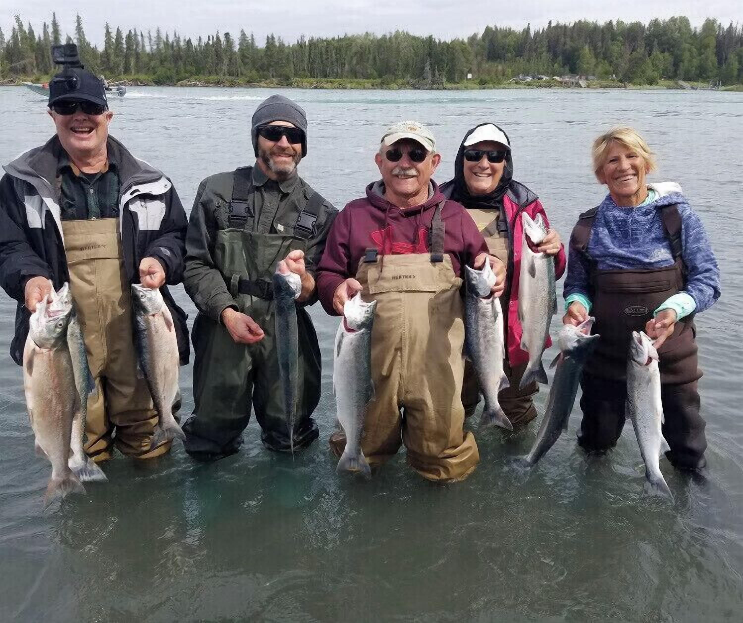 A group of people standing in a body of water, holding fish.