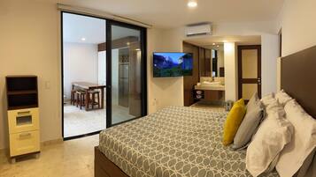 Un dormitorio con cama, televisor, baño y puerta corrediza de vidrio a un balcón.