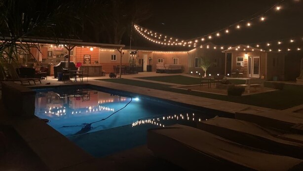 A swimming pool with a string of lights above, surrounded by a house and a lawn. - Private country studio, near SMF and UC Davis Campus (Woodland)