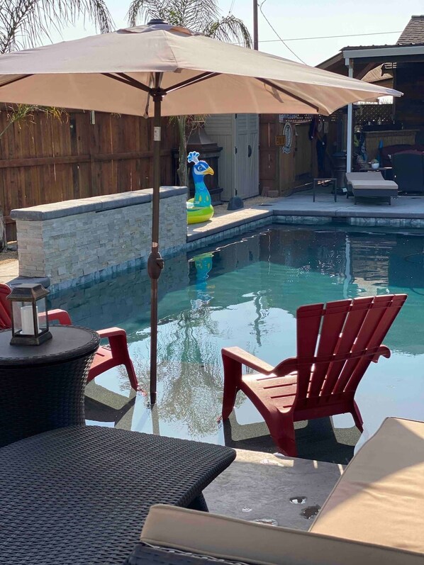 Un patio trasero con piscina, sillas rojas, una mesa con un farol y una valla de madera.