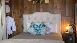 A bedroom with a tufted headboard, a bed with patterned pillows, a bedside table with a lamp, and a wooden wardrobe with towels. - Private country studio, near SMF and UC Davis Campus (Woodland)