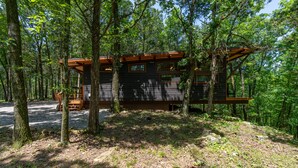 A cabin in a forest with a deck and a covered picnic table.