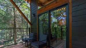 A wooden deck with a glass door leading to a forested area.