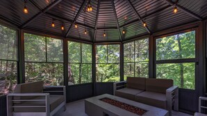 A conservatory with a modern design, featuring a built-in fire pit, seating areas, and large windows offering views of the surrounding forest.