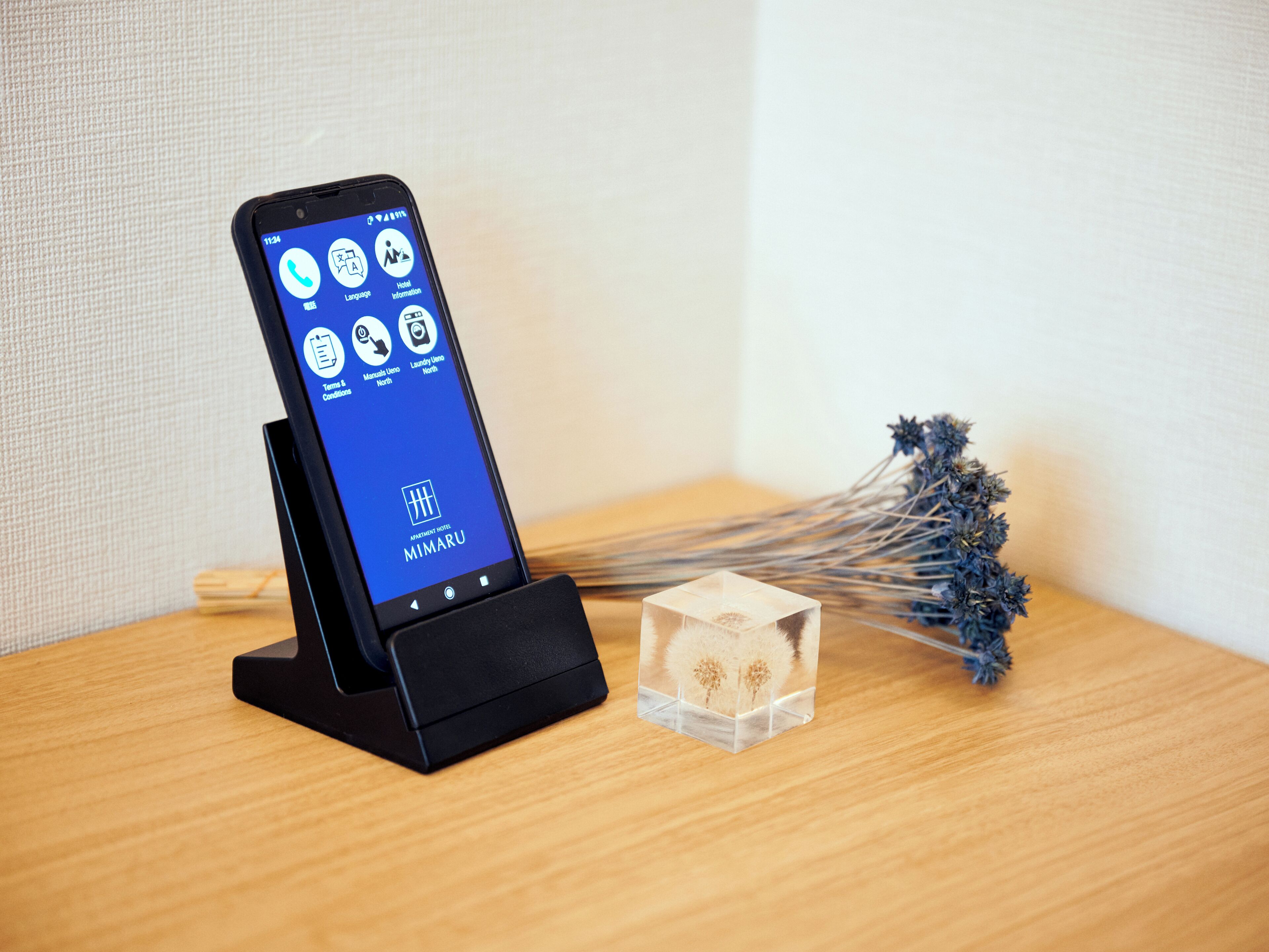 En smartphone ligger i en laddningsstation och visar en hotellapp med funktioner som språkval, information om hotellet och information om rummen.